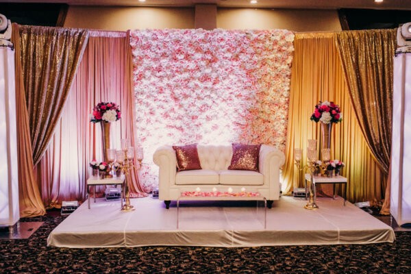 White couch decorated with sparkling pink pillows stands before a wall with flowers and waits for newlyweds